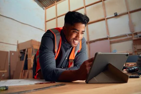 Young man smiling while working on digital tablet next to tools in woodworking Stock Photos