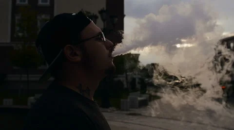 Young Man Smoke E-Cigarette On Street At Sunset. Vape. Slow-Mo. Video stock 65039434