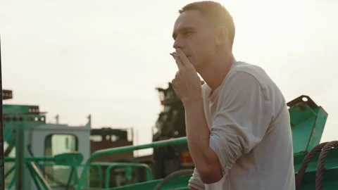 A young man smokes a cigarette. medium shot. Day, outdoor shot. low angle Stock Footage 252672892
