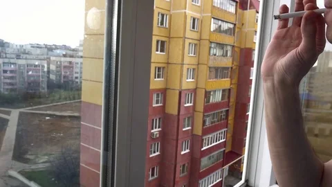 Young man smokes a cigarette at the window Stock Footage 74751707