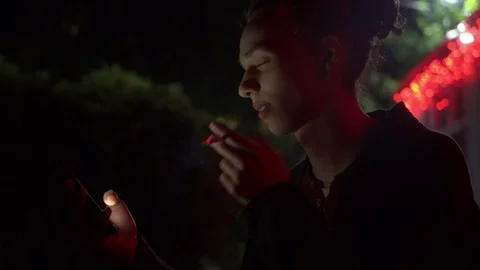 Young man smoking and using smartphone outdoors at night 2 Video stock 95863887