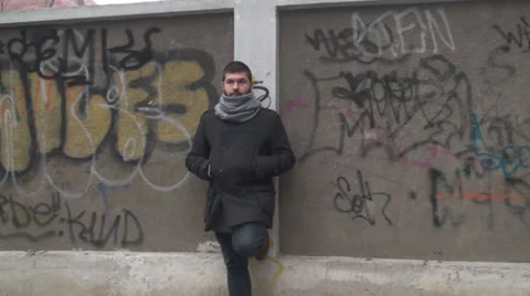 Young Man Smoking A Cigar While Waiting In Front Of A Graffiti Fence Stock-Footage 33654916