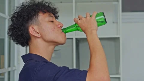 Young man smoking cigarette while drinking alcohol from green bottle Stock Footage 332389061