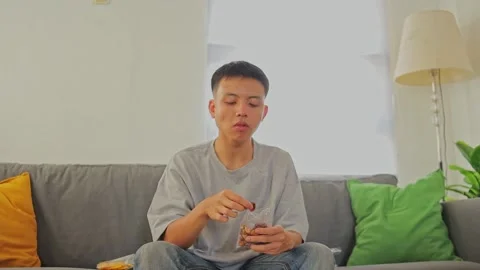 Young man Snacking on roasted nuts while sit on cozy sofa Stock Footage 346264985