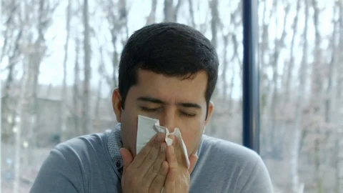 Young man sneezing in front of a window Stock Footage 101792498