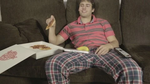Young man on the sofa eating pizza and watching TV Stock Footage 46261142