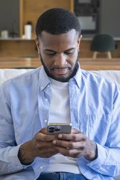 Young man on a sofa focused on his smartphone, texting and browsing in a re.. Stock Photos
