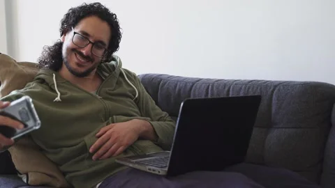 Young man on the sofa taking selfie while using laptop Stock Footage 164906259