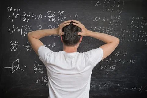 Young man is solving mathematical problem on blackboard and is confused. Stock Photos