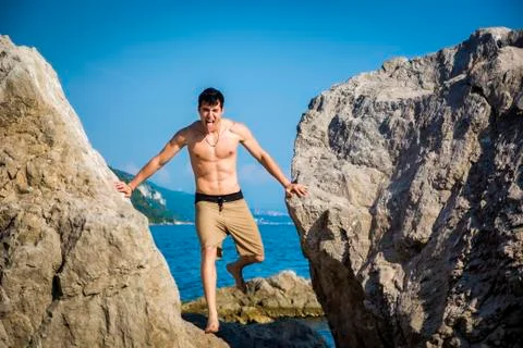Young Man Spanning Gap Between Coastal Boulders Stock Photos