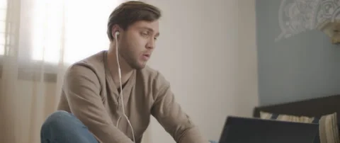 A young man speaking to someone through earphones while working on his laptop Stock Footage 135096297