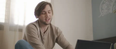 A young man speaking to someone through earphones while working on his laptop Stock Footage 135096488