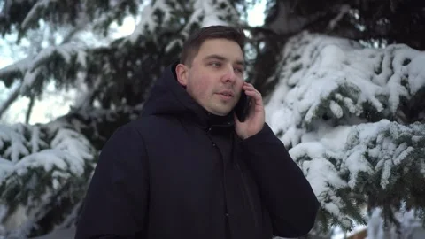 A young man speaks on the phone while standing against a background of spruce in Stock-Footage 266330112