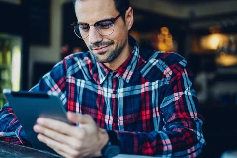 Young man in spectacles watching network videos on modern touch pad device Stock Photos