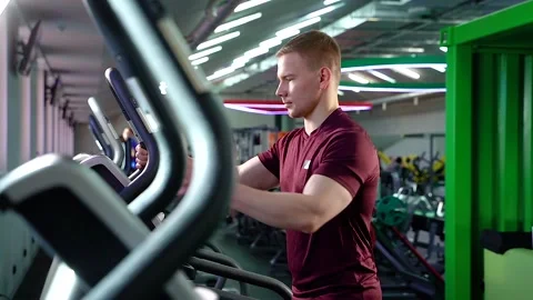Young man in sportswear using elliptical machine and doing cardio workout in gym Stock Footage 100978741