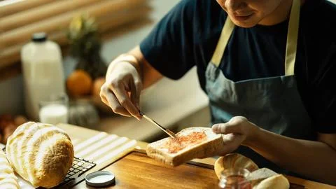 Young man spreading sweet raspberry jam on bread during for breakfast or brunch Stock Photos