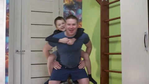 A young man squats with his son on his back. fitness classes. sports at home Stock Footage 170784104
