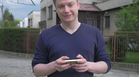 Young man standing and using mobile phone. He looks into the camera. Stock Footage 62519175