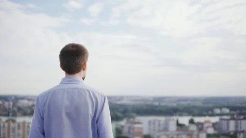 Young man standing on the balcony looking at a landscape with a view of the city Stock Footage 129184774