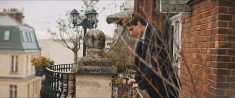 Young man standing on a balcony looking down the street Stock Footage 203587020