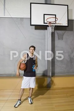 A young man standing on a basketball court holding a sports drink and a Stock Photos