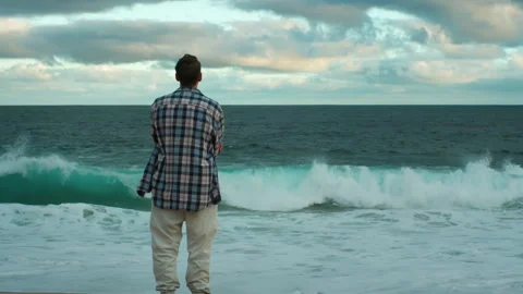 Young man standing on a beach looking towards the ocean horizon Vidéo 317944402