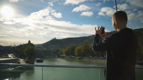 Young man standing on the beautiful bridge and taking a photo slow motion Stock Footage 70815570