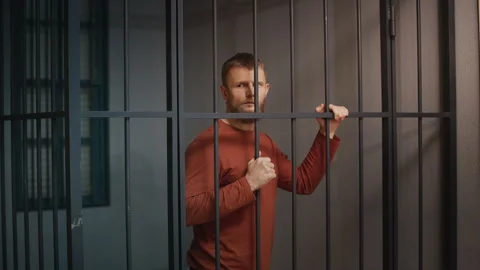Young man standing behind jail cell bars after arrest for a minor offense Stock Footage 340031180