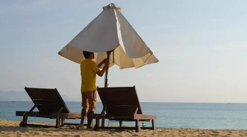 Young man standing bitween beach loungers and opening an umbrella. Back view Stock-Footage 62599358