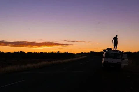 Young man standing on car while a nice Sunset in the Outback of Australia, no Foto stock