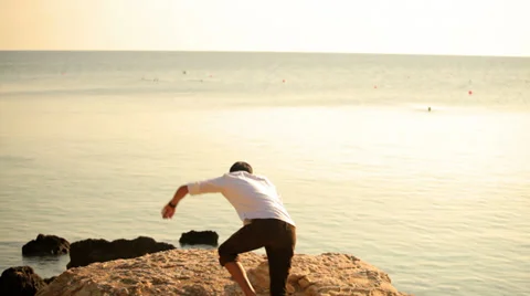 A young man standing on a cliff looking out into the ocean during magic hour Stock Footage 33847675