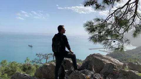 Young man standing at a cliff overlooking at ponoramic view of sea Vidéo 149252066