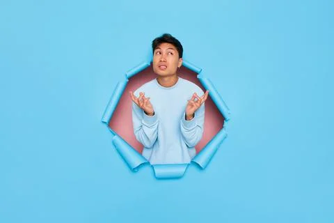 Young man standing in cutout of blue backdrop, looks up and calculates options Stock-Fotos