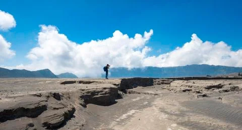 Young man is standing at an earth splinter and photographed smoking volcano Photos