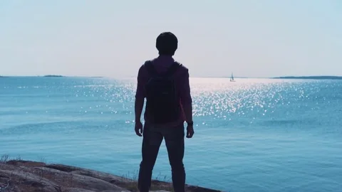 Young man standing on edge of ocean cliff looking into the distance at the sea Stockbeeldmateriaal 80669279