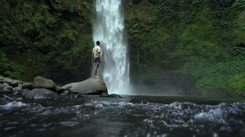 Young man standing in front of powerful waterfall in rain forest. Stock Footage 126778877