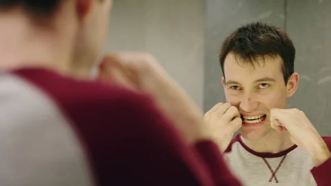 Young man standing in front of a round LED mirror, carefully flossing his teeth Stock Footage 312274653
