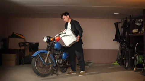 Young man standing in a garage, pouring fuel from a metal gas can into the tank Stock Footage 342774875