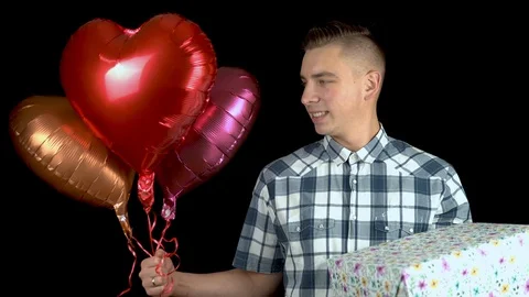 A young man is standing with a gift and heart-shaped balloons. A man holds in Stock Footage 122114249