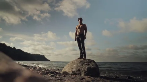 A young man is standing on a large rock on the beach. Stock Footage 78708047
