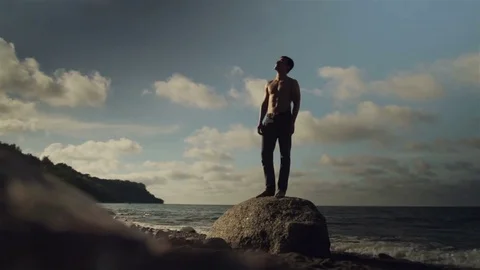 A young man is standing on a large rock on the beach. Stock Footage 78712072