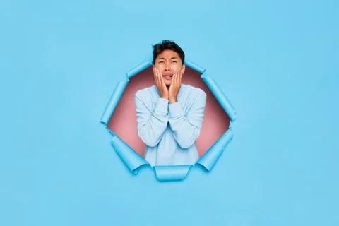 Young man standing in middle cutout of blue background, very upset, pressing his Stock Photos