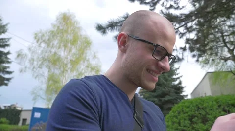 Young man standing with mobile phone in the park. Then he starts walking. Video stock 62519959
