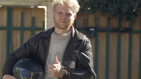 A young man standing next to his motorcycle gives a thumbs up Stock Footage 72363892