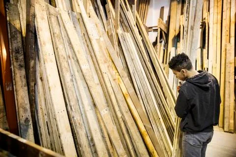 Young man standing next to a stack of wooden planks in a warehouse. Stockfoto's