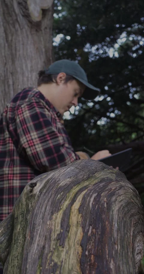 Young man standing peacefully under a large tree, journaling in a notebook. Stock Footage 313950010