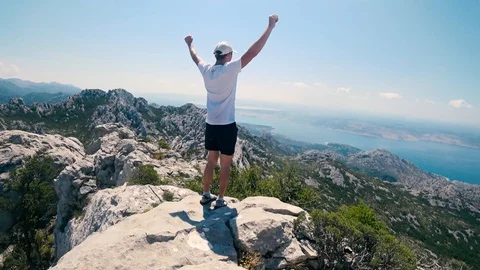 Young man standing on the peak of the mountain rising hands up celebrating Stock Footage 114222012
