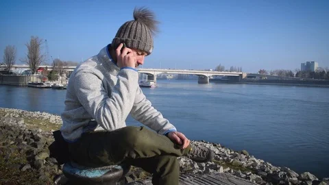 Young man standing on the riverside and talking on cellphone Stock Footage 70887838