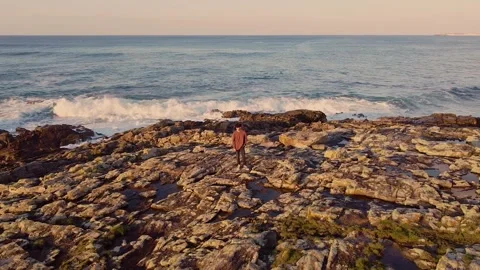 Young Man Standing On The Rocky Cliffs With Rough Sea Waves. Pullback Shot Stock Footage 243818291
