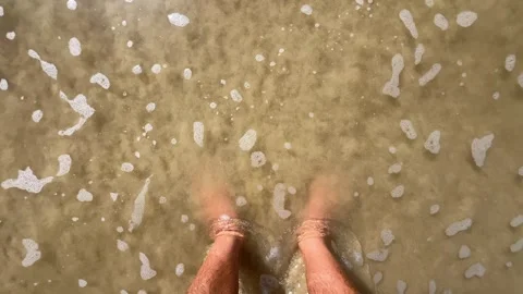 Young man standing on the sand of the beach with the sea water touching his feet Video stock 320228754